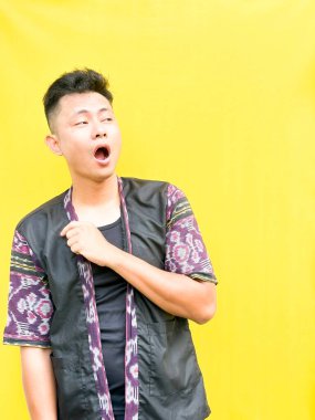 Modern etnik esinlenilmiş bir kıyafet giyen genç bir Asyalı 'nın portresi, parlak sarı bir arkaplan önünde dururken şüpheli ya da meraklı bir görünüm veriyor. Duygular, ruh hali ifadesi gibi kavramlar için mükemmel..