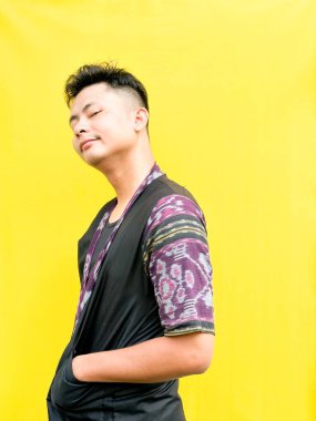 Modern etnik esinlenilmiş bir kıyafet giyen genç bir Asyalı 'nın portresi, parlak sarı bir arkaplan önünde dururken şüpheli ya da meraklı bir görünüm veriyor. Duygular, ruh hali ifadesi gibi kavramlar için mükemmel..