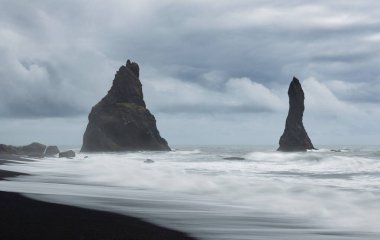 Güney İzlanda 'da, rüzgarlı, bulutlu bir günde ve dalgalı denizde Reinisdrangar kıyılarının ve deniz yığınlarının uzun pozu.