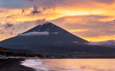 Amed köyü, Bali, Endonezya 'da siyah kumsalda renkli bir gün batımı ve arka planda agung volkanı.