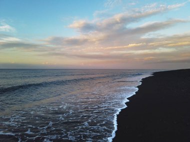 Kara kum plajı, Amed, Bali, Endonezya 'da dalgalar ve gün batımı