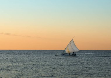 Günbatımında okyanusta yelkenli.
