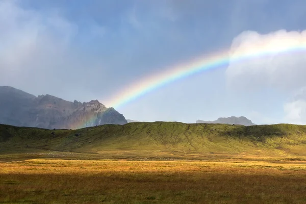 Rainbow in the clouds over the sunny hills in highlands of Iceland