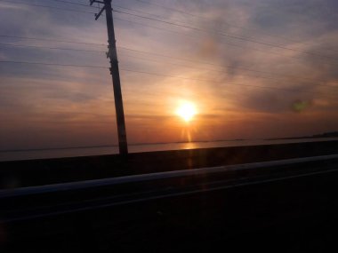 Gün batımına karşı kablolarla yol, nehir ve direk.