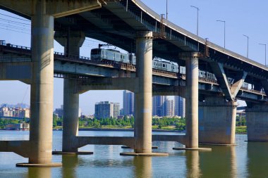Seul, Güney Kore - 2 Haziran 2023: Bir metro treni, Han Nehri üzerindeki Cheongdam Köprüsü 'nün alt güvertesinden geçmekte ve altında belirgin beton sütunlar bulunmaktadır..