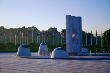Seul, Güney Kore - 2 Haziran 2023: Olimpiyat Parkı 'nda çarpıcı beton heykel, arka planda rakip ülkelerin bayrakları dalgalanıyor.