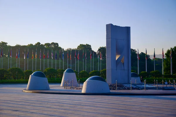 stock image Seoul, South Korea - June 2, 2023: A striking concrete sculpture in Olympic Park, with a row of flags from competing nations fluttering in the background.