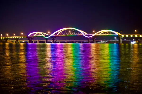 Over the South Han River, South Korea - February 20, 2020: The Tangeum Grand Bridge radiates with a dazzling display of rainbow colors, reflecting off the river\'s surface at night.
