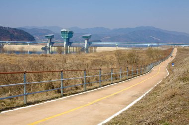 Gumi Şehri, Güney Kore - 9 Mart 2017: Gumi Weir yakınlarındaki uzun bisiklet yolunun manzaralı bir uzantısı, uzakta ve görkemli dağların arka planında, modern altyapının ve doğal güzelliğin harmanlanmasının bir örneği..
