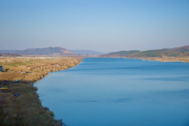 Sangju Şehri, Güney Kore - 18 Kasım 2023: Geniş Nakdong Nehri 'nin geniş bir manzarası, bitişiğindeki tarım alanları ve alçak tepeleri, geniş Kore gökyüzü altında doğal ve tarımsal manzaralardan oluşan huzurlu bir duvar halısı yaratıyor..