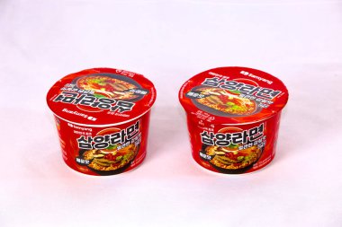 Ulsan, Güney Kore - 14 Ocak 2024: Samyang 'ın iki paket baharatlı umami ramen' i yuvarlak bardaklarda, koyu kırmızı ambalajda, beyaz bir zemin üzerine kurulmuş bu popüler hazır baharatlı rameni vurguluyor..