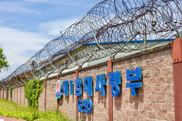Город Донхэ, Южная Корея - 28 июля 2019 года: Высокая стена, увенчанная колючей проволокой, окружает порт Донхэ под ясным голубым небом. Знак, установленный на стене, обозначает границу этой охраняемой зоны..
