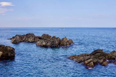 Donghae Şehri, Güney Kore - 28 Temmuz 2019: Kayalar Eodal Limanı yakınlarındaki sakin Doğu Denizi sularının üzerinde, açık mavi bir gökyüzü ve mavi suyun altında uzanan ufukta görünen bir balıkçı teknesi, bu güneşli yaz gününde görülebilen bir balıkçı teknesi..