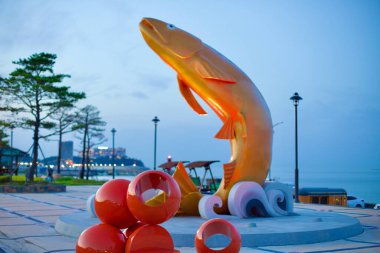 Yangyang İlçesi, Güney Kore - 30 Temmuz 2019 Golden Somon Park 'ta sudan fırlayan 10 metrelik çarpıcı bir somon heykeli, gün batımından sonra tabanda balık yumurtasıyla kırmızıya boyandı..