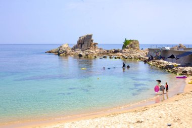 Goseong İlçesi, Güney Kore - 30 Temmuz 2019 Gonghyeonjin Limanı yakınlarındaki Gonghyeonjin Sahili ziyaretçilerin dalış ve şnorkelle dalmayı sevdiği kum ve kristal berrak sularıyla büyülenir. Arka planda, ilginç bir kaya koleksiyonu iki taya çıkıyor.