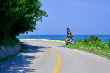 Goseong County, South Korea - July 31, 2019: An empty road with distinctive blue lines marking the bike path, stretches from Hwajinpo Beach to Chodo Beach, offering breathtaking views of the East Sea under a clear blue sky. clipart