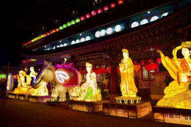 Ulsan, Güney Kore - 15 Mayıs 2024: Jeonggwangsa Tapınağı 'nın girişinin önünde 2 metre boyunda parlayan Budist figürler. Orta Buda 'nın tepesinde bir fil fenerler ve üzerinde Kore bayrağı sembolleri olan dairesel ışıklarla çevrilidir.