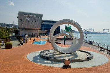 Ulsan, Güney Kore - 17 Mart 2024: Jangsaengpo Balina Müzesi 'nin modern akvaryumunun arka planında heykeller bulunur ve küçük bir limanın sularına bakar. Geniş bir kırmızı tuğla avlu davetkar atmosfere ekleniyor.