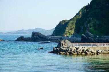 Gangneung Şehri, Güney Kore - 18 Mayıs 2024: Heonhwa Yolu Doğu Denizi 'nin kayalık kıyı şeridi boyunca esiyor. Engebeli kayalıklar ve beton dalga kırıcılar sakin ve berrak sulara çarpıcı bir tezat oluşturuyor..