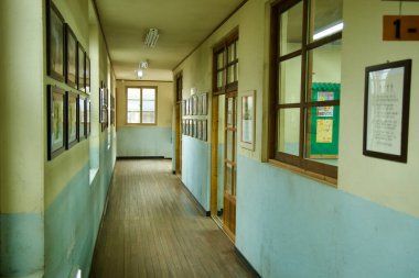 Ulsan, Güney Kore - 17 Mart 2024: Jangsaengpo Balina Kültür Köyü 'nde ahşap zemin, eski sınıf pencereleri ve çerçeveli fotoğrafların yer aldığı bir okul koridorunun nostaljik görüntüsü. Bu sahne 20. yüzyılın ortasındaki K 'nin özünü yakalar.