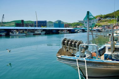 Samcheok City, Güney Kore - 18 Mayıs 2024: Samcheok Limanında arka planda sanayi binaları bulunan balıkçı tekneleri, limanın hem yerel hem de endüstriyel faaliyetleri destekleyen ikili rolünü gözler önüne seriyor.