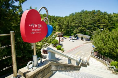 Samcheok City, Güney Kore - 18 Mayıs 2024: Merdivenler, kalp şeklinde bir işaret ve çevreleyen yeşilliğin manzaralı bir manzarasının yer aldığı Yeni Milenyum Sahil Lunaparkı 'na iniyor. Park eğlence faaliyetleri ve güzel bir ortam sunuyor.