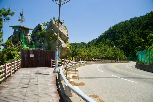 stock image Samcheok City, South Korea - May 18, 2024: A notable bend in Isabu Road featuring a unique rock formation and adjacent observation area, surrounded by lush greenery and forested hills.