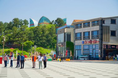 Donghae Şehri, Güney Kore - 18 Mayıs 2024: Bir grup turist Chuam Sahili yakınlarındaki canlı meydanı keşfediyor, çevrede dükkanlar ve kafeler ve yemyeşil alanlar bulunuyor.