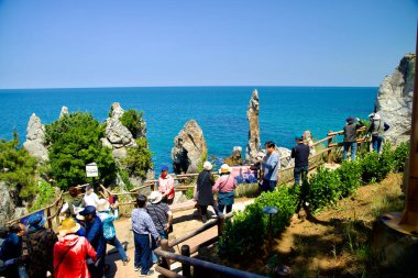 Donghae City, South Korea - May 18th, 2024: Tourists gather to view and photograph the iconic Chuam Candlestick Rock along the coast of the East Sea. This popular natural landmark, known for its unique rock formations, draws visitors for its scenic b clipart