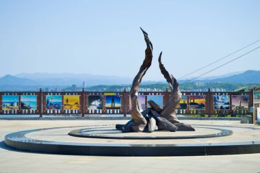 Donghae, Güney Kore - 18 Mayıs 2024: Mukho Deniz Feneri 'nin altındaki avluda çarpıcı bir yangın heykeli duruyor, canlı fotoğraf görüntüleriyle çevrili ve şehrin ve dağların panoramik manzarasını sunuyor..