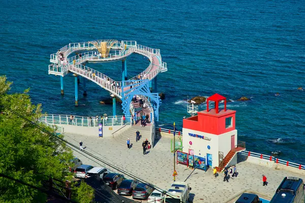 stock image Donghae City, South Korea - May 18th, 2024: The Dojebigol Haerang Observatory extends over the East Sea, offering scenic views, with the red lighthouse adding a vibrant touch to the coastal area.