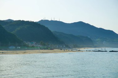 Gangneung, Güney Kore - 18 Mayıs 2024: Jeongdongjin Sahili 'nin sakin manzarası, kıyı şeridi boyunca uzanan kumlu kıyıları ve arka plandaki dağları, ziyaretçiler bölgenin doğal güzelliğinin tadını çıkarırken.