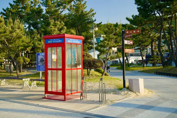 stock image Gangneung, South Korea - May 18th, 2024: A bright red Jeongdongjin Certification Center stands ready to serve bicycle tourists. This booth, located in a scenic park setting near the beach, provides an essential stop for cyclists exploring the area, o