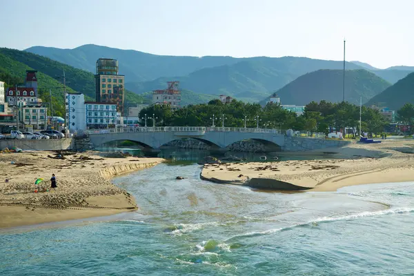 Gangneung, Güney Kore - 18 Mayıs 2024 Jeongdongjin Sahili 'nden geçen bir akarsu manzarası, şehir ve dağlarla birlikte büyüleyici bir köprünün altından geçen manzaralı bir zemin.