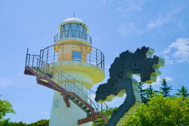 Uljin County, South Korea - July 27th, 2024: A detailed close-up of Hupo Lighthouse, highlighting its weathered structure alongside a modern abstract sculpture, set against a clear summer sky. clipart