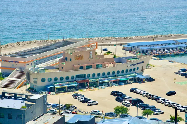 stock image Uljin County, South Korea - July 27th, 2024: An aerial view of the Hupo Fisheries Cooperative Distribution Center, a ship-shaped building at Hupo Port, bustling with activity as it facilitates the distribution of locally caught seafood along Korea's 