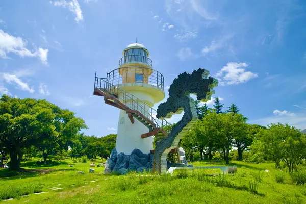 stock image Uljin County, South Korea - July 27th, 2024: A close-up view of Hupo Lighthouse at Deunggi Mountain Park, featuring a modern, abstract sculpture set against a backdrop of lush green trees and a clear blue sky.