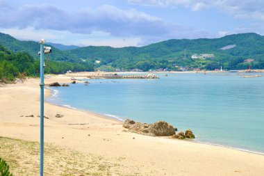 Samcheok, Güney Kore - 29 Temmuz 2024: Uzaklara uzanan kumlu kıyı şeridi, sakin tepeler ve turkuaz sularla çevrili, huzurlu bir kıyı manzarası oluşturan Wonpyeong Sahili geniş bir manzara.