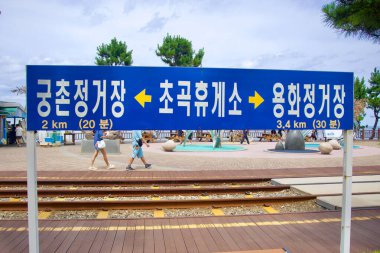 Samcheok, Güney Kore - 29 Temmuz 2024: Samcheok Demiryolu Bisiklet Pisti 'nin yakınındaki Chogok Dinlenme Tesisi' nin dışında, Gungchon ve Yonghwa İstasyonları 'na olan mesafeyi ve arka planda ziyaretçileri ve kıyı şeridini gösteren bir işaret..