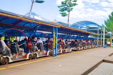 Samcheok, South Korea - July 29, 2024: Tourists prepare to depart on the Samcheok Marine Rail Bike from Gungchon Station, as multiple four-seater bikes are lined up under a covered platform on a bright summer day. clipart