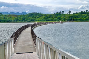 Sokcho, South Korea - July 28th, 2024: The curved pontoon bridge at Yeongnang Lake stretches across calm waters, offering a scenic route for walkers and cyclists, surrounded by lush greenery and distant mountains. clipart