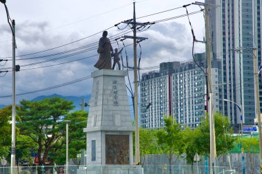 Sokcho City, South Korea - July 28th, 2024: A front view of the Restoration Memorial Tower featuring a statue of a mother and child looking northward. The monument honors the refugees displaced by the Korean War, set against the backdrop of Sokcho's  clipart