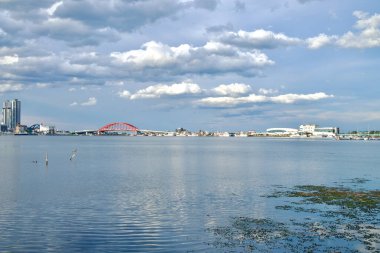 Sokcho, Güney Kore - 28 Temmuz 2024: Seorak Grand Köprüsü 'nün Cheongcho Gölü üzerindeki kırmızı kemerlerinin geniş panoramik manzarası, Sokcho' nun modern deniz kıyısındaki binaları ve tesisleri ufuk boyunca parçalı bulutlu bir gökyüzü altında uzanıyor..