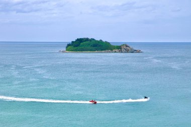 Goseong County, Güney Kore - 28 Temmuz 2024: Bir jet ski ve muz teknesi, Geumgu Adası yakınlarındaki sakin sularda hızla ilerliyor, Doğu Denizi 'nde küçük, yemyeşil bir ada, sakin doğal bir zemine karşı heyecan verici su sporları sunuyor..