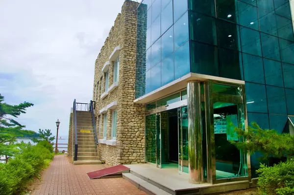 stock image Goseong County, South Korea - July 28, 2024: The entrance to Kim Il-Sung's Villa combines modern glass architecture with the historic stone facade, leading visitors into the iconic villa surrounded by lush greenery at Hwajinpo Lake.