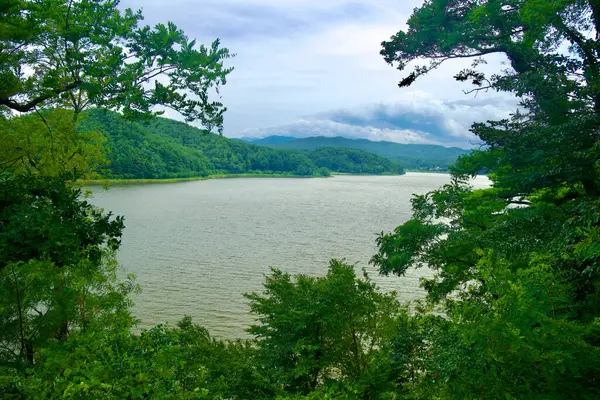 stock image Goseong County, South Korea - July 28th, 2024: A breathtaking view of Hwajinpo Lake, surrounded by lush green mountains and trees, as seen from the vantage point of Syngman Rhee's historic cottage in Goseong County.