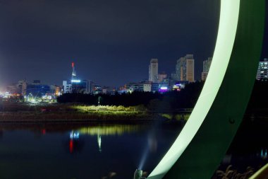 Ulsan, Güney Kore - 12 Aralık 2019: Taehwa Nehri üzerindeki Simnidaebat Köprüsü 'nün aydınlatılmış desteğinin yakın görüntüsü, şehrin ufuk çizgisi ve geceleri Taehwa Nehri Ulusal Bahçesi' nin yansımaları..