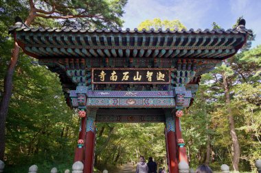 Ulsan, South Korea - October 21st, 2023: A detailed view of the intricately designed entrance gate to Seoknamsa Temple, featuring vibrant woodwork and calligraphy, framed by the lush surrounding forest. clipart