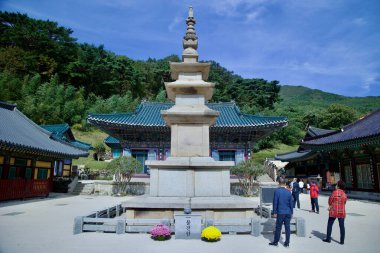 Ulsan, South Korea - October 21st, 2023: A stone pagoda stands prominently in the courtyard of Seoknamsa Temple, surrounded by vibrant temple buildings and autumn foliage, as visitors explore the serene grounds. clipart