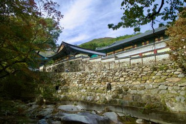 Ulsan, South Korea - October 22nd, 2023: The stone wall along Seoknamsa Temple, overlooking a gentle creek, with the building's traditional architecture blending into the surrounding nature. clipart